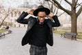 Outdoor photo of slim african man having fun in spring park. Portrait of enthusiastic brunette black guy in hat dancing