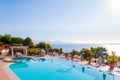 Outdoor pool with vibrant crystal water, parasols and deck chairs located on the coast of Garda with lake, hills and sun on Royalty Free Stock Photo