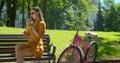 Outdoor portrait of attractive young woman with a bicycle drinking lemonade on a park bench. Fashionable young woman has Royalty Free Stock Photo