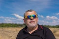 Outdoor portrait of a bearded senior in sunglasses against blue cloudy sky