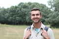 Outdoor portrait in of beautiful happy handsome young man smiling and laughing with perfect teeth hiking with black rucksack Royalty Free Stock Photo