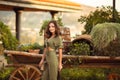 Outdoor Portrait of beautiful woman smiling with curly hair style enjoying at park by wooden cart with green grass and flowers.