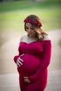Outdoor portrait of a beautiful young mother to be holding her maternity belly wearing long flowing red dress
