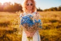 Outdoor portrait of beautiful young woman with red curly hair holding bouquet of flowers. Summer mood. Royalty Free Stock Photo