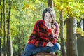 Outdoor portrait of cheerful young woman sitting on sawn tree trunk