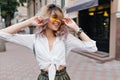 Outdoor portrait of cheerful young woman in vintage white shirt and yellow glasses carrying elegant silver backpack Royalty Free Stock Photo