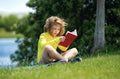 Outdoor portrait of a cute little kid reading a book in summer park. Blond kid boy sitting on grass and reading book Royalty Free Stock Photo