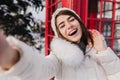 Outdoor portrait of cute woman with happy smile making selfie in London during winter vacation. Adorable girl in white