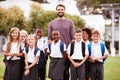 Outdoor Portrait Of Elementary School Pupils With Teacher Wearing Uniform Standing On Playing Field