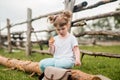 Outdoor portrait of a girl sitting on the grass near the fence.Summer in the village. beautiful baby girl on a wooden bench. Royalty Free Stock Photo