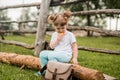 Outdoor portrait of a girl sitting on the grass near the fence.Summer in the village. beautiful baby girl on a wooden bench. Royalty Free Stock Photo