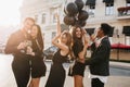 Outdoor portrait of glad students in stylish attires dancing on the street with balloons, celebrating graduation