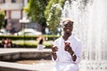 Portrait of handsome afro american young man listening music from phone drinking coffee to go on summer street in front of fountai Royalty Free Stock Photo