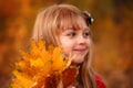 Outdoor portrait of happy blonde child girl in a red jacket holding yellow leaves. Little girl walking in the autumn park or Royalty Free Stock Photo