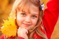 Outdoor portrait of happy blonde child girl in a red jacket holding yellow leaves. Little girl walking in the autumn park or Royalty Free Stock Photo
