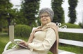 Portrait of a happy senior lady sitting on a park bench and using her laptop computer Royalty Free Stock Photo