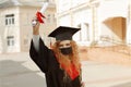 Happy grad student, she is in a black mortarboard with red tassel, and a face mask, in gown shows a diploma in her hand Royalty Free Stock Photo