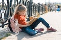 Outdoor portrait of little schoolgirl with book, girl child 7, 8 years old with glasses backpack reading textbook Royalty Free Stock Photo