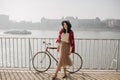 Outdoor portrait of lovable girl in beige skirt standing near bicycle. Full-length photo of well-dressed young woman in