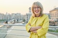 Outdoor portrait of mature smiling woman with glasses, yellow raincoat. Woman 40, 45 years old, spring city background, copy space Royalty Free Stock Photo