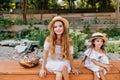 Outdoor portrait of pleased young woman and girl sitting with legs crossed in park on nature background after picnic