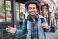 Outdoor portrait of positive african-american with afro hairstyle waving and smiling at camera while walking in street Royalty Free Stock Photo