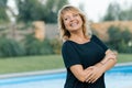 Outdoor portrait of positive confident mature woman. Smiling female blonde with arms crossed, background of pool, private Royalty Free Stock Photo