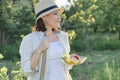 Outdoor portrait of positive mature woman in straw hat. Smiling female with plate of strawberries mint lemon, background green Royalty Free Stock Photo