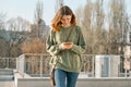 Outdoor portrait of pretty teen girl walking and texting on mobile phone, spring sunny day background Royalty Free Stock Photo