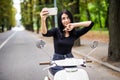 Outdoor portrait of pretty young woman sitting on scooter taking selfie on her smart phone. Royalty Free Stock Photo