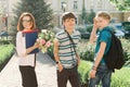 Outdoor portrait of school teacher with bouquet of flowers and group of teenage school children. Children congratulate their