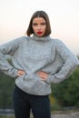 Outdoor portrait of a stylish tanned girl wearing knitted sweater posing on a street