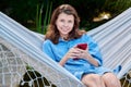 Outdoor portrait of teenage girl sitting in hammock with smartphone Royalty Free Stock Photo