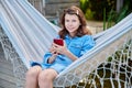 Outdoor portrait of teenage girl sitting in hammock with smartphone Royalty Free Stock Photo