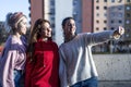 Outdoor portrait of three friends fun girls taking photos with a smartphone at bright sunset. Group of happy women taking self-