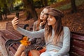 Outdoor portrait of two young women taking selfie using phone. Girls having fun in autumn park. Best friends Royalty Free Stock Photo