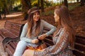 Outdoor portrait of two young women talking sitting on bench in autumn park. Friends hang out together Royalty Free Stock Photo