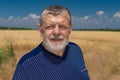 Ortrait of Ukrainian bearded Caucasian senior farmer against crop field and blue sky