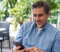 Outdoor portrait of white man using phone on a terrace, checking e-mails, reading news feed, posting on social media