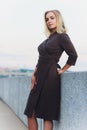 Outdoor portrait of young beautiful caucasuan woman with long straight hair in short black dress, beige shoes holding Royalty Free Stock Photo