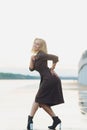 Outdoor portrait of young beautiful caucasuan woman with long straight hair in short black dress, beige shoes holding Royalty Free Stock Photo