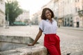 Outdoor portrait of young beautiful confident fashionable African lady, leaning on the stone city fountain, posing to Royalty Free Stock Photo