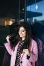 Outdoor portrait of a young beautiful fashionable woman walking on the street. Model wearing stylish pink coat, black Royalty Free Stock Photo