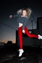 Outdoor portrait of young beautiful happy blond european lady posing on street at night. Model wearing stylish clothes red pants a Royalty Free Stock Photo