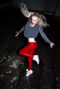 Outdoor portrait of young beautiful happy blond european lady posing on street at night. Model wearing stylish clothes red pants a Royalty Free Stock Photo