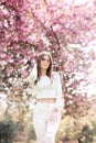 Outdoor portrait of young beautiful happy smiling lady posing near flowering tree. Model wearing stylish accessories Royalty Free Stock Photo