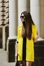 Outdoor portrait of young beautiful lady walking on the street. Model wearing sunglasses and stylish yellow summer dress Royalty Free Stock Photo