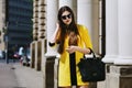 Outdoor portrait of young beautiful lady walking on the street. Model wearing sunglasses and stylish yellow summer dress Royalty Free Stock Photo