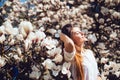 Outdoor portrait of a young beautiful woman near magnolia tree with flowers get sun bath. Girl wearing stylish clothes. Female spr Royalty Free Stock Photo