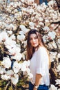 Outdoor portrait of a young beautiful woman near magnolia tree with flowers. Girl wearing stylish clothes. Female spring mood Royalty Free Stock Photo